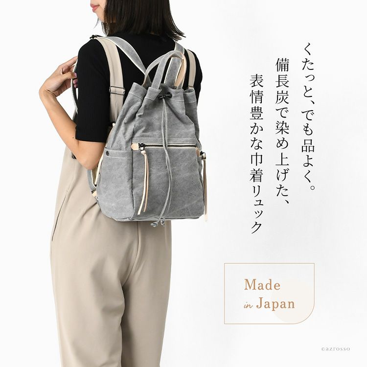 軽量で畳める日本製巾着リュックを背負う女性モデル。帆布素材で大容量、A4収納可。背面ファスナー直結やサイドポケットで機能的なレディースリュック
